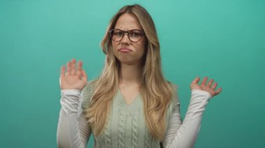 Gözlük takan sarışın kadın, parlak bir fotoğraf stüdyosunda avuç içlerini açıyor; belirsizlik şüpheciliği.