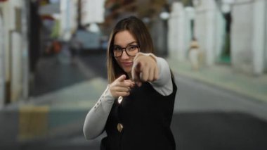 Gözlüklü genç sarışın kadın, neşeli ve çekici bir atmosferi somutlaştıran açık hava ortamını neşeyle işaret ediyor..