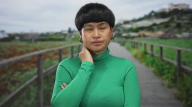 Çevresi doğa ile çevrili, yeşil bir parkta duygularını ifade eden bir kadın düşünceli ve düşünceli tavrını vurguluyor..