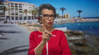 Okyanus manzaralı deniz kenarında gezinti yapmayan, gözlüklü gri saçlı, canlı kırmızı elbiseli, canlı bir sahil manzarası olan bir kadın..