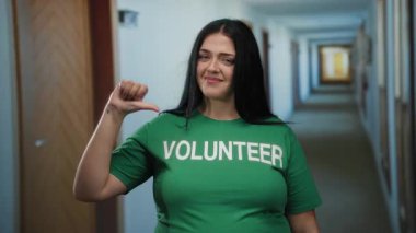 Yeşil gönüllü gömlekli bir kadın otel koridorunda duruyor. Kendine güvenen kıvrımlı, neşeli, genç, sıradan bir kadın ve otel koridoru çevresi pozitif..