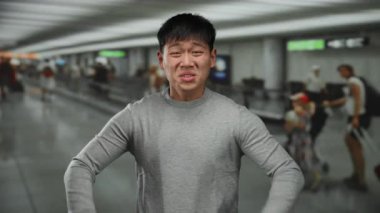 Havaalanı terminalinde hayal kırıklığını ifade eden genç bir adam. Etrafı bulanık yolcularla çevrili. Seyahat stresi ve yoğun bir ev ortamını aktarıyor..