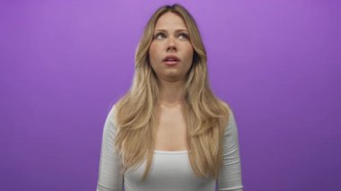 Uzun saçlı sarışın kadın, mor stüdyo ortamında elini kaldırarak silah hareketi yapıyor. Sinir bozucu iğneleme..