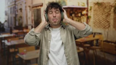 İspanyol bir adam, bir sokak restoranının terasında kulaklıkla müzik dinlemekten hoşlanıyor. Şehir arka planında rahat ve yakışıklı görünüyor..