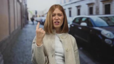 Sarışın, bej hırka giyen genç bir kadın kaldırım taşı caddesinde sıkılmış yumruğunu kaldırıyor..