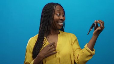 Gülümseyen ve elinde arabanın anahtarı olan bir kadın mavi izole edilmiş arka planda, yüzünde heyecan ve mutluluk olan sarı bir gömlek giyiyor..