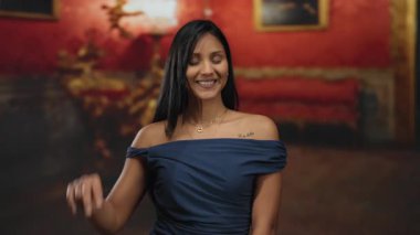 Müzede canlı kırmızı ve altın desenli barış işareti yapan, zarif mavi elbiseler giyen, sakince gülümseyen, sakin bir anı yakalayan bir kadın..