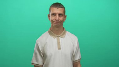 Yeşil arka planda umursamazlığını ifade eden bir adam eliyle işaret ederken, izole bir duvara karşı bej bir gömlek giyiyor..