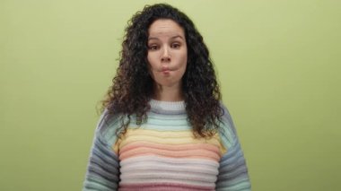 Kıvırcık saçlı İspanyol bir kadın, yumuşak sarı bir arka plana karşı neşeli bir balık yüzü takınıyor. Renkli bir kazak giyiyor..