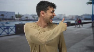 Baş parmağı havada bir adam açık hava manzarası gösterir. Mutlu, genç, İspanyol bir gülümseme..