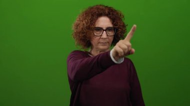 Yeşil duvara odaklanmış, gözlük ve süveter takan, izole bir ortamda kararlılık ve vurgu gösteren bir kadın..