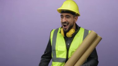 Miğfer ve güvenlik yeleği giyen genç adam, mor bir arkaplan önünde sürpriz bir ifadeyle planları elinde tutuyor..