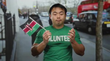 Kentsel sokak ortamında yeşil gönüllü tişörtü giymiş Kenya bayrağını tutan genç adam, şehir telaşıyla çevrili yüzünde düşünceli ama kafası karışmış bir ifade beliriyor..