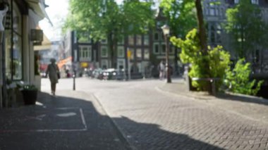 Amsterdam 'daki bulanık şehir manzarası. Ağaçların ve tarihi binaların arasında kaldırım taşından kaldırımda yürüyen bir kadın. Güneş ışığı altında, bokeh atmosferinde..