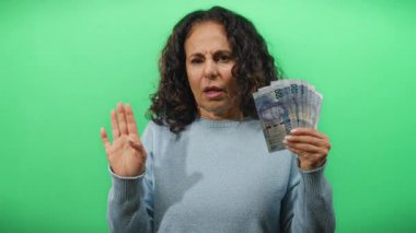 Güney Afrika banknotlarını elinde tutan orta yaşlı bir kadın izole edilmiş yeşil arka plan duvarına karşı şaşırmış bir ifadeyle para birimi ve ekonomik kavramları vurguluyor..