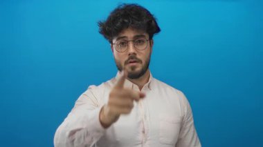 Sakallı ve gözlüklü genç İspanyol bir adam canlı mavi bir arkaplan önünde jestler yapıyor, bir dizi dinamik pozlarla yön, odak ve karar ifadelerini vurguluyor..