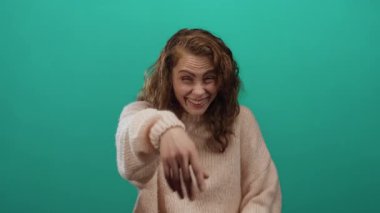 Yeşil bir arka plan önünde neşeli bir şekilde gülen, rahat bir kazak giyen, mutluluk ve kaygısız duyguları ifade eden, samimi bir kahkaha anında yakalanan bir kadın..