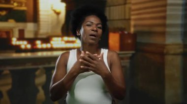 Kilisedeki kadın ellerini göğsüne yapıştırarak duygularını ifade ediyor. Arka plan aydınlanmış. Kapalı bir ortam ve canlı bir ortam izlenimi veriyor..