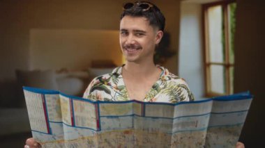 Yatak odasında haritası olan tropikal gömlek giyen genç adam pencereden güneş ışığıyla gülümsüyor. Geziye hazırlanmayı ve dışarıda macera yaşamayı öneriyor.