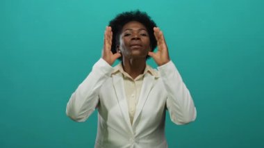 İzole edilmiş yeşil arka plana karşı tutkuyla bağıran bir kadın beyaz takım elbise giyiyor, elleri ağızda ifade ediyor, iletişim kuruyor, duygu kuruyor..