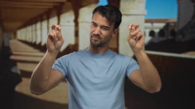 Mavi gömlekli genç İspanyol, güneşli bir gökyüzünün altındaki açık hava üniversitesinde özgüvenle tırnak işareti yapıyor..