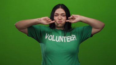 Yeşil arka planda neşeli bir şekilde poz veren yeşil gönüllü bir kadın, kıvrımlı ve gençlik ruhunu sıradan ve dostane bir şekilde somutlaştırıyor..