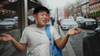 Mavi sırt çantalı genç adam hareketli bir şehir caddesinde, şehir dışında belirsizlik ya da tereddüt taşıyor..