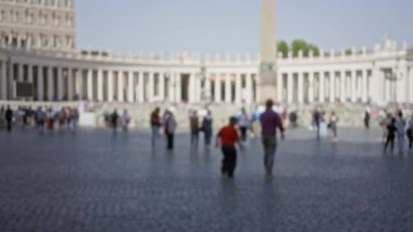 Bulanık kalabalık St. Peter Meydanı, Vatikan 'da güneşli gökyüzünün altında kaldırım taşında yürüyor, ikonik sütunları ve dikilitaşları çekiyor..