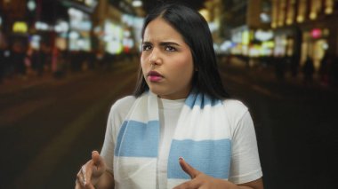 Dışarıda parmaklarını sayan bir kadın var. Yoğun bir caddede arka planı bulanık. Beyaz tişört ve mavi eşarp giyiyor..