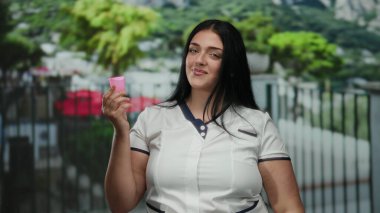 Çevresel farkındalığı vurgulayan canlı kentsel bir ortamda, canlı bir şehir arka planında pembe bir adet bardağını tutan bir kadın gülümsüyor.