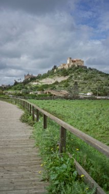 Arta, Mallorca 'daki tarihi bir tepe kalesine giden yol yemyeşil ve bulutlu gökyüzü ile çevrili, Akdeniz manzarası ve mimarisi sergileniyor..