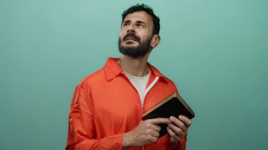 Turuncu hapishane tulumu giymiş İspanyol bir adam yeşil bir arka plana karşı İncil tutuyor. Hapisteki inanç ve yansımayı sembolize ediyor..