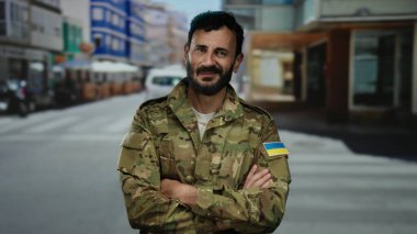 Ukrayna bayraklı askeri üniformalı bir adam açık bir şehir caddesinde güvenle duruyor..