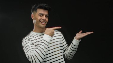 Şık çizgili tişörtlü İspanyol bir adam. Siyah bir arka plana karşı özgüvenle el kol hareketi yapıyor. Zarafet ve çekicilik taşıyor..