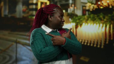 Kandille aydınlatılmış bir kilise ortamında kollarını çapraz gösteren kadın, Afrika kökenli Amerikalı kökenli ve canlı saçlı, düşünce ya da karar önerisinde bulunuyor..