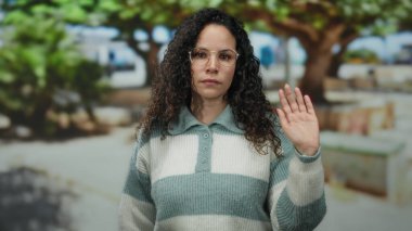 Parkta gözlüklü ve çizgili süveter giyen, güneşli bir günde ağaçlarla çevrili, rahat bir ortamda güneşli bir anı canlandıran bir kadın..