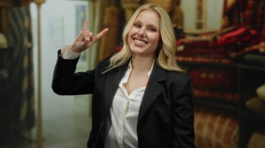 Etrafı renkli tekstil ürünleriyle çevrili bir dekor dükkanında taş işareti yapan bir kadın neşeli bir havayı işaret ediyor..