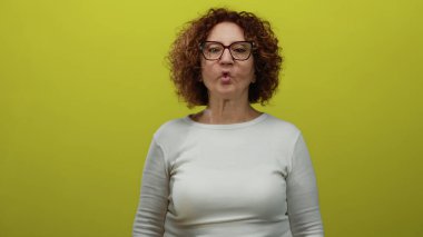 Middle-aged hispanic woman with glasses posing against a vibrant yellow background, expressing an animated facial gesture.
