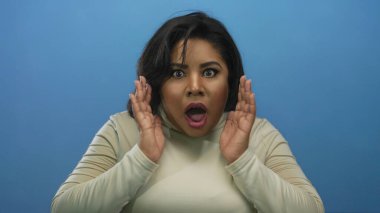 Genç, iri yarı, İspanyol bir kadın mavi izole bir arka planda şaşkınlık yaşıyor..