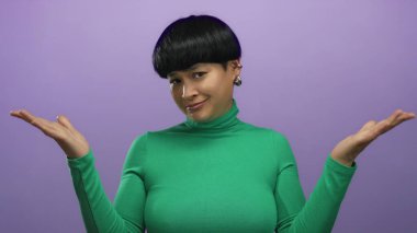 Yeşil elbiseli kadın, izole edilmiş mor arka plana şüpheyle yaklaşıyor. Kısa saçlı ve eşsiz küpeleri var. Minimalist arka planla çelişiyor..