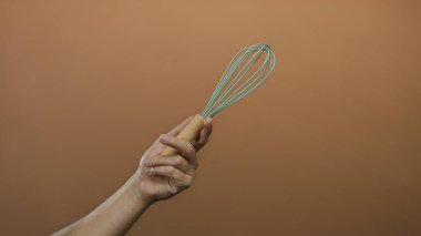 Kahverengi duvar arka planında yeşil çırpı tutan bir adam, beyaz erkek eli ve çatal bıçak üzerinde münferit odaklı minimalist bir ortamda mutfak aletlerini sergiliyor..