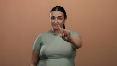 Hayır diyen bir kadın, kahverengi bir arka planda, kendine güvenen genç ve iri yarı bir kadının ifadesini izole bir ortamda yakalıyor..