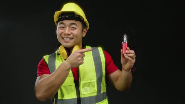 Kasklı ve güvenlik yeleği olan gülümseyen inşaatçı elinde siyah arka plan aydınlatma cihazıyla ürünü vurguluyor.