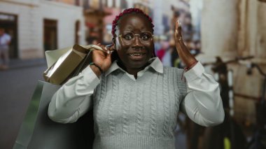 Şehrin sokaklarında elinde alışveriş torbalarıyla gülümseyen bir kadın, şehir yaşam tarzı ve tüketiciliğini gözler önüne seriyor..