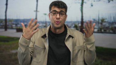 Genç İspanyol gözlüklü adam siyah bir gömleğin üstüne düz ceket giyerken adam marina kaldırımında omuz silkip ceketini kaldırıyor..