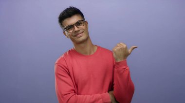 Gözlüklü ve kırmızı gömlekli genç adam mor arka planda duruyor. Ayrı bir ortamda başparmak hareketlerini güven ve cazibeyle gösteriyor.