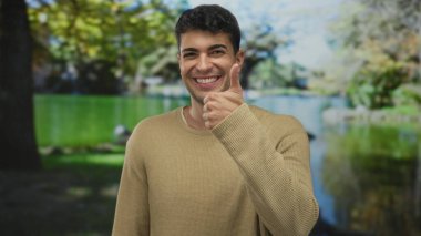 Dışarıyı gösteren genç, İspanyol asıllı, gülümseyen, parkın arka planında pozitif enerji var..