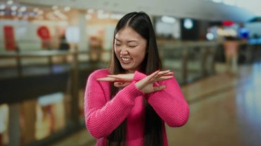 Pembe kazaklı kadın hareketli bir alışveriş merkezinde, modern bir alışveriş merkezinde Asyalı güzellik ve cazibesini sergiliyor..