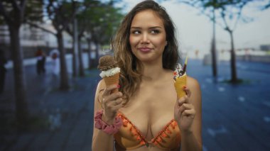 Açık havada güneşli bir sokakta canlı bir bikiniyle dondurma yiyen bir kadın, gençlik coşkusu ve coşkuyla dolu neşeli bir yaz sahnesini vurguluyor..