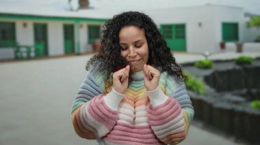 Arka planda evler, mutluluk ve doğal güzellik saçan günlük bir sokak sahnesinde renkli bir süveter giyen kadın..